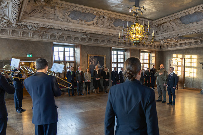 Umerov and Jonson stands at attention in a large fancy ball room as the national anthems are performed by a military marching band.