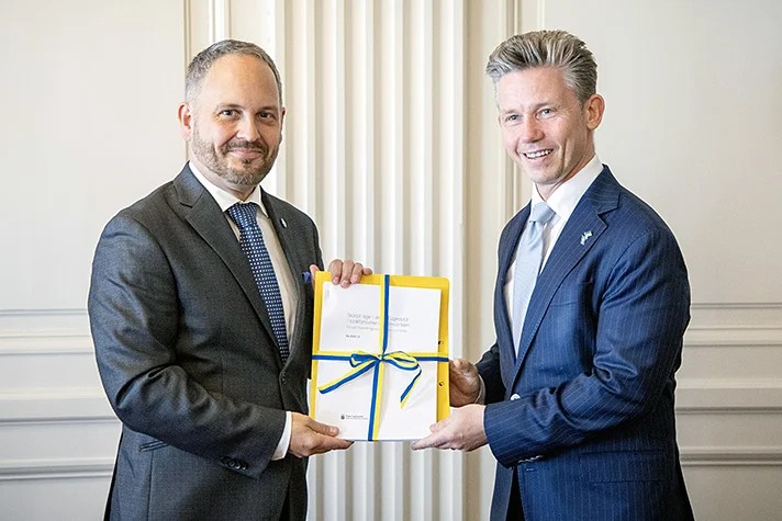 Jörgen Berglund and Pål Jonson are standing next to each other. Jonson recieve a report in his hands.