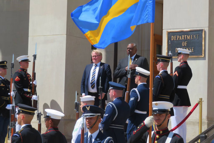 Peter Hultqvist and Lloyd Austin standing outside surrounded by soldiers and a Swedish flag.