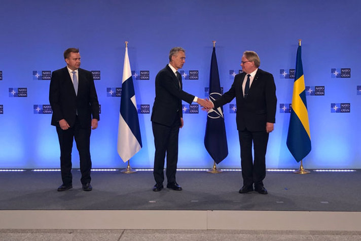 Jens Stoltenberg shaking hands with Peter Hultqvist while Antti Kaikkonen is watching.
