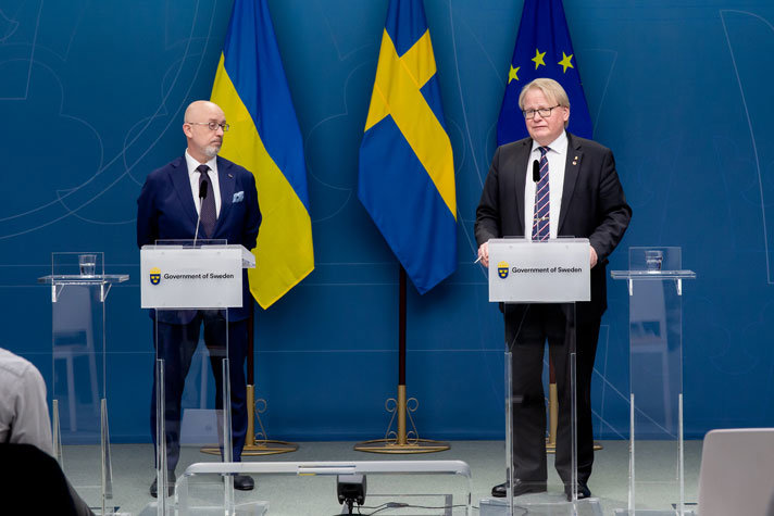 Peter Hultqvist and Oleksii Reznikov in suits in front of microphones at a press conference.